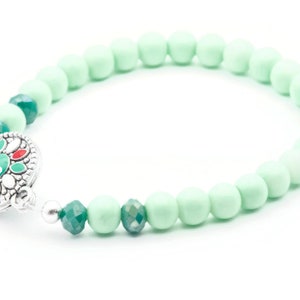 May include: A mint green beaded bracelet with a silver clasp featuring a green and red floral design.