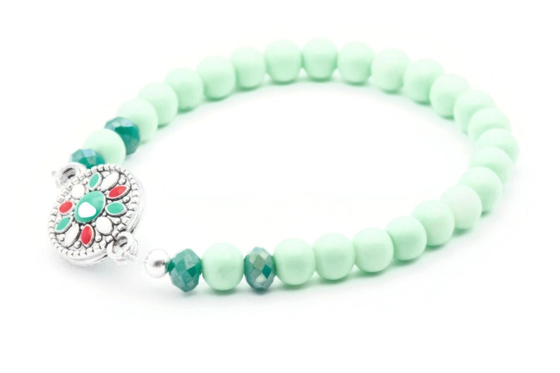 May include: A mint green beaded bracelet with a silver clasp featuring a green and red floral design.