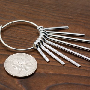 Puede incluir: Pendientes de aro de plata con un dise&ntilde;o en forma de abanico de m&uacute;ltiples varillas de plata unidas al aro.