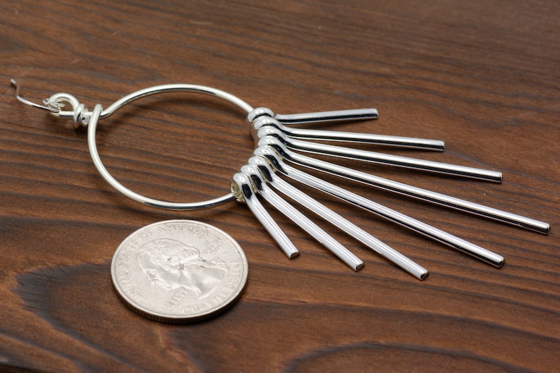 Puede incluir: Pendientes de aro de plata con un dise&ntilde;o en forma de abanico de m&uacute;ltiples varillas de plata unidas al aro.