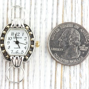 Peut inclure: Une montre &agrave; quartz Geneva argent&eacute;e et dor&eacute;e avec un cadran blanc et des chiffres noirs. La montre a un petit cadran ovale avec une lunette d&eacute;corative et une couronne dor&eacute;e. Une pi&egrave;ce de 25 cents am&eacute;ricaine est &agrave; c&ocirc;t&eacute; de la montre pour la comparaison de taille.