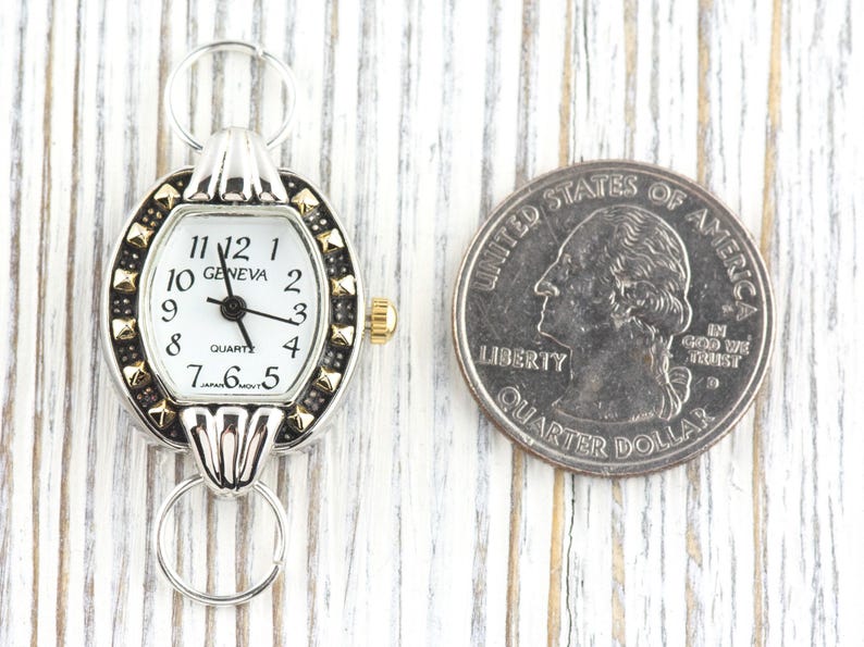 Peut inclure: Une montre &agrave; quartz Geneva argent&eacute;e et dor&eacute;e avec un cadran blanc et des chiffres noirs. La montre a un petit cadran ovale avec une lunette d&eacute;corative et une couronne dor&eacute;e. Une pi&egrave;ce de 25 cents am&eacute;ricaine est &agrave; c&ocirc;t&eacute; de la montre pour la comparaison de taille.