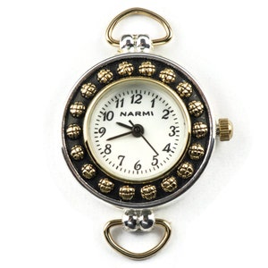 May include: A silver and gold tone watch with a white face and black numbers. The watch has a decorative bezel with gold accents and a loop for attaching to a chain.
