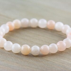 Op de afbeelding: Een armband gemaakt van witte en roze edelsteen kralen. De kralen zijn rond en glad, en de armband is geregen op een doorzichtig elastisch koord.