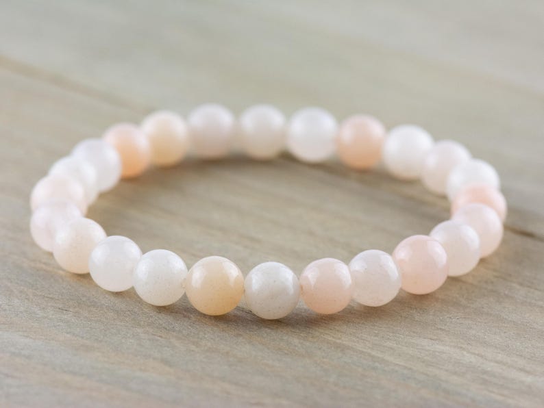 Op de afbeelding: Een armband gemaakt van witte en roze edelsteen kralen. De kralen zijn rond en glad, en de armband is geregen op een doorzichtig elastisch koord.