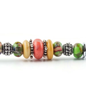 May include: A close-up of a colourful beaded bracelet with a silver end cap. The bracelet features a variety of round beads in shades of green, orange, and pink, interspersed with silver spacer beads.