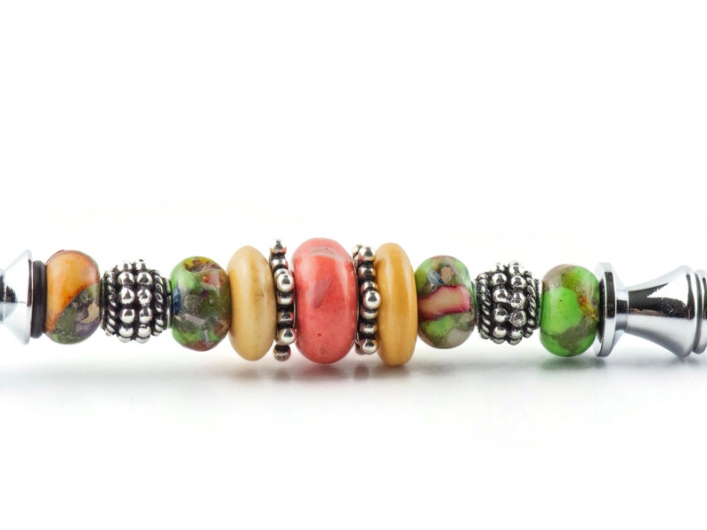 May include: A close-up of a colourful beaded bracelet with a silver end cap. The bracelet features a variety of round beads in shades of green, orange, and pink, interspersed with silver spacer beads.