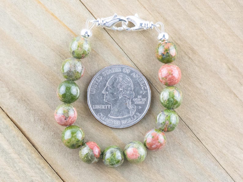 Puede incluir: Un brazalete de piedras preciosas verdes y rosas con un cierre plateado. El brazalete est&aacute; hecho de cuentas redondas y tiene aproximadamente el tama&ntilde;o de una moneda de 25 c&eacute;ntimos de euro.