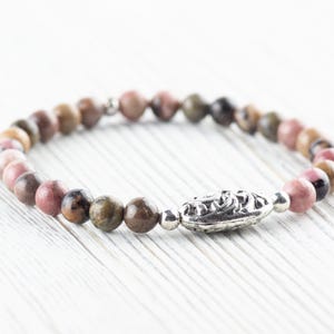 Puede incluir: Un brazalete de piedras preciosas rosa, marr&oacute;n y verde con un cierre plateado. El brazalete est&aacute; hecho de peque&ntilde;as cuentas redondas.