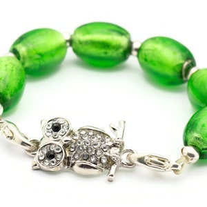 May include: A green glass bead bracelet with an owl charm. The owl charm is silver and has rhinestones for eyes.