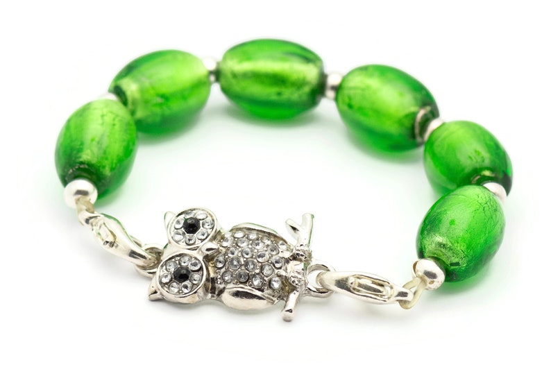 May include: A green glass bead bracelet with an owl charm. The owl charm is silver and has rhinestones for eyes.