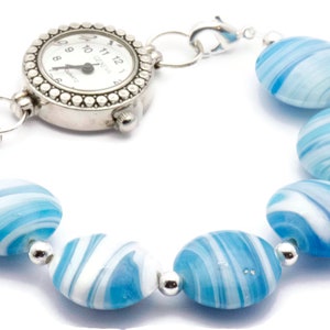May include: A silver watch with a white face and black hands attached to a bracelet made of blue and white swirl glass beads.