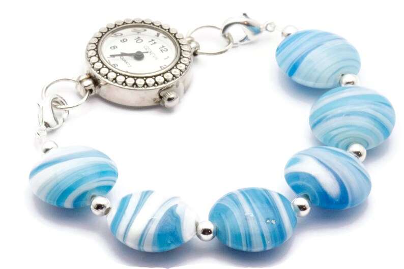 May include: A silver watch with a white face and black hands attached to a bracelet made of blue and white swirl glass beads.