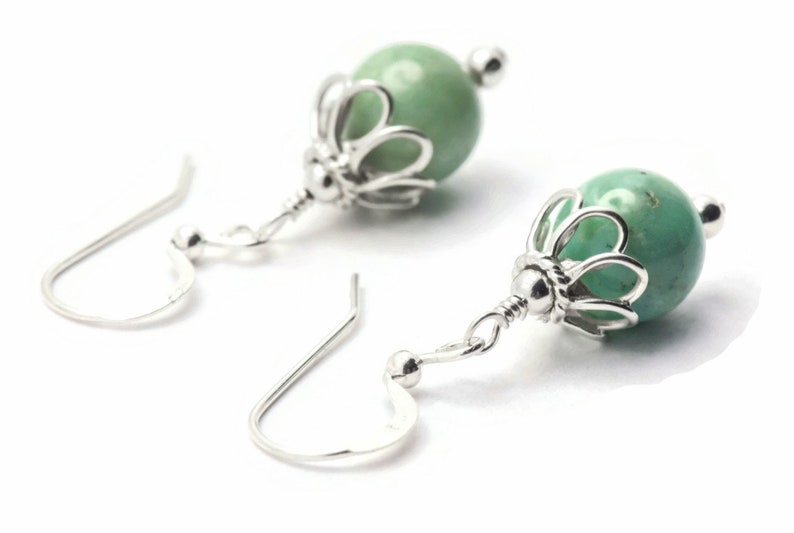Puede incluir: Un par de pendientes de plata con cuentas de piedras preciosas verdes y un delicado dise&ntilde;o floral.