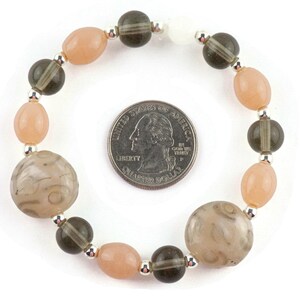May include: A bracelet made with light pink and dark grey beads. The bracelet is about the size of a UK 20 pence coin.