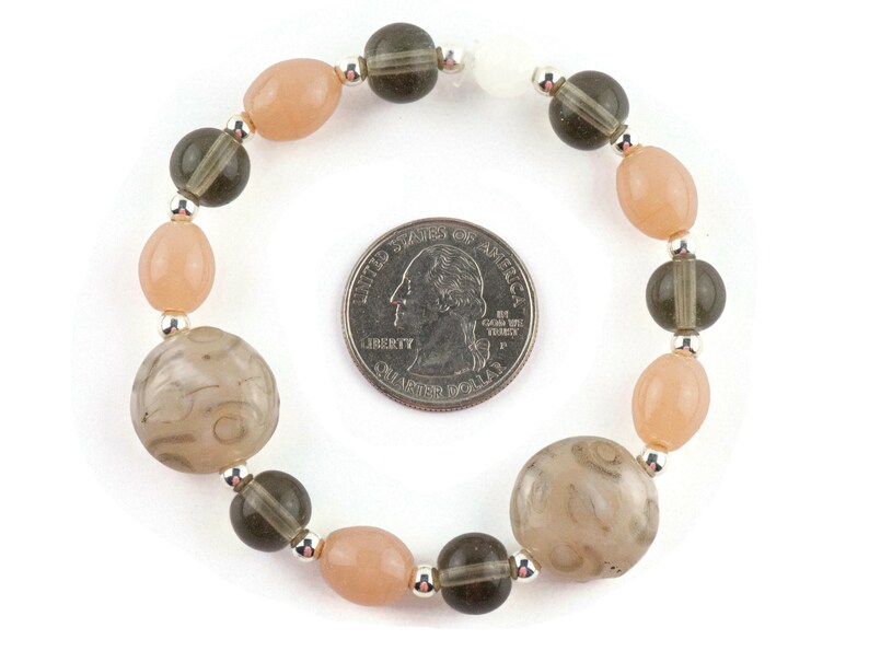 May include: A bracelet made with light pink and dark grey beads. The bracelet is about the size of a UK 20 pence coin.