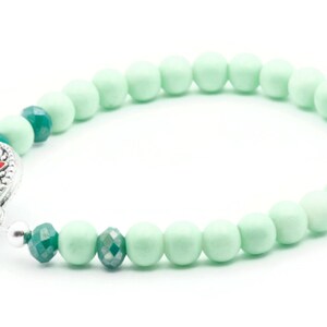May include: A green and silver beaded bracelet with a decorative clasp. The bracelet is made of round beads with a smooth finish.