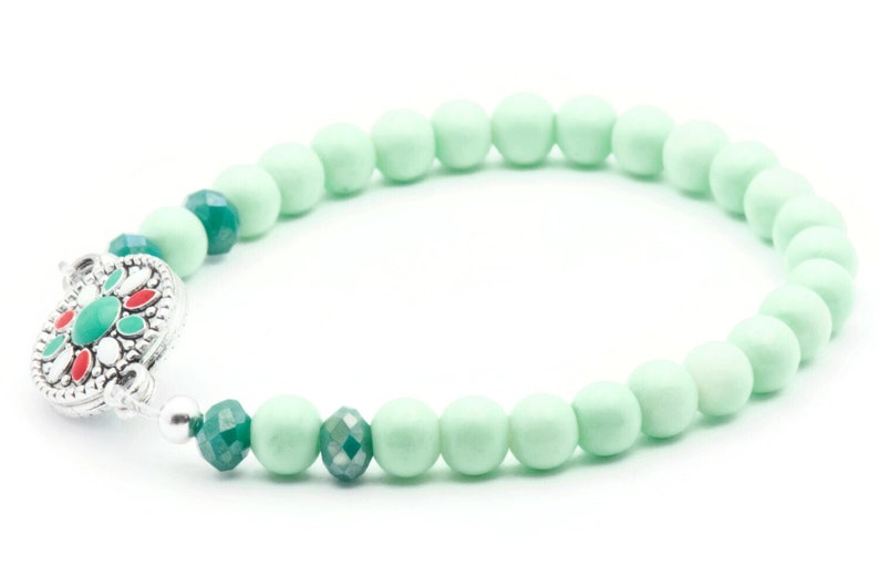 May include: A green and silver beaded bracelet with a decorative clasp. The bracelet is made of round beads with a smooth finish.