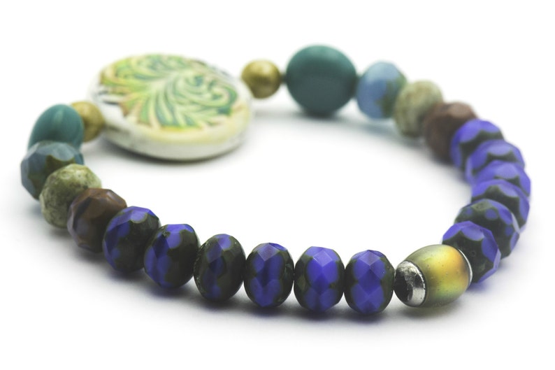 Puede incluir: Un brazalete de cuentas azules y verdes con un dije de cer&aacute;mica con un dise&ntilde;o de hojas.