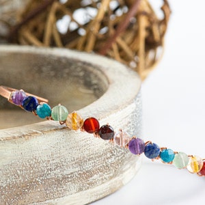 K&ouml;nnte beinhalten: Ein Kupferdraht-Armband mit bunten runden Perlen. Die Perlen sind in einem Regenbogenmuster angeordnet, beginnend mit Lila und endend mit Gr&uuml;n.
