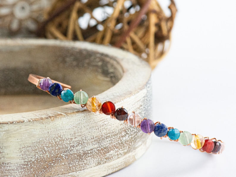 K&ouml;nnte beinhalten: Ein Kupferdraht-Armband mit bunten runden Perlen. Die Perlen sind in einem Regenbogenmuster angeordnet, beginnend mit Lila und endend mit Gr&uuml;n.
