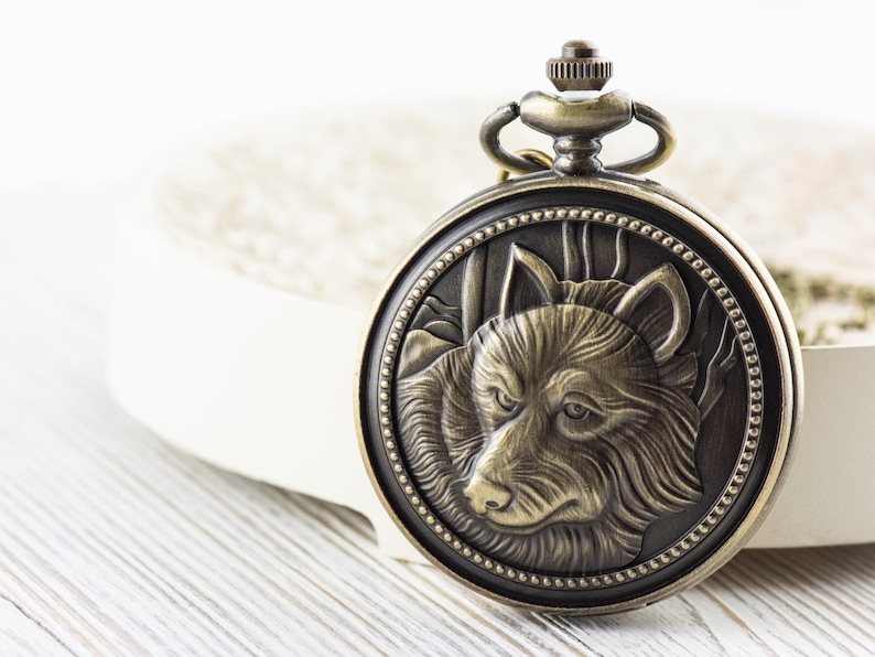 May include: A vintage-style pocket watch with a detailed wolf head design on the face. The watch is made of brass and has a chain attached.