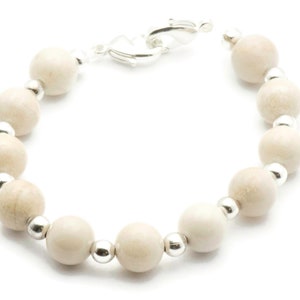 Op de afbeelding: Een armband van witte houten kralen met zilveren accenten. De armband heeft een sluiting.