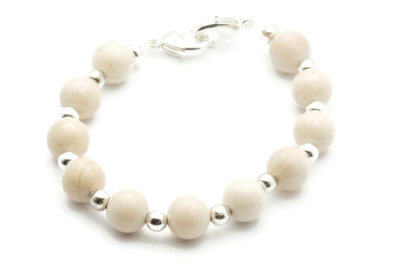 Op de afbeelding: Een armband van witte houten kralen met zilveren accenten. De armband heeft een sluiting.