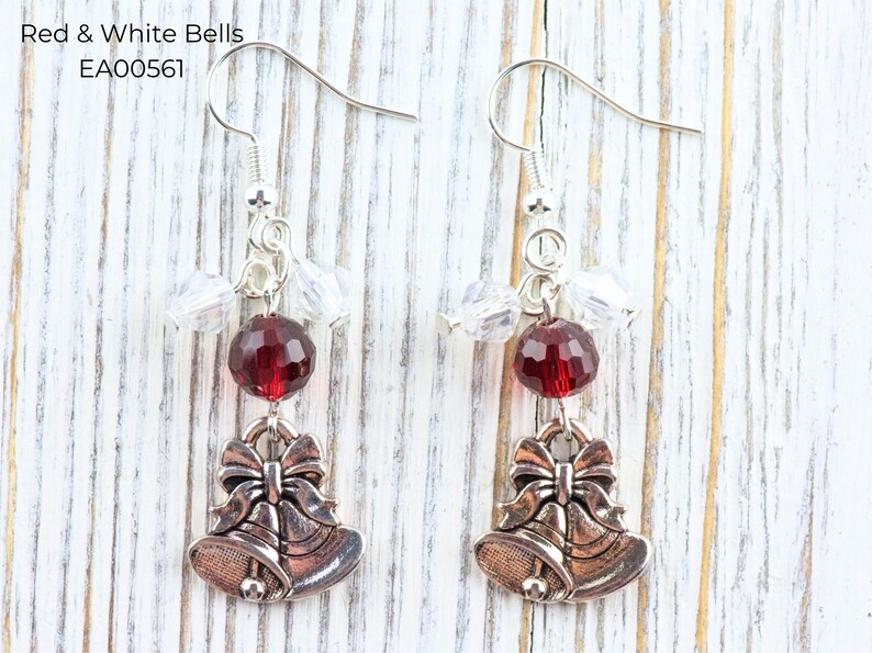 Pode incluir: Brincos pendurados prateados com uma conta facetada vermelha e contas de cristal transparentes. Cada brinco tem um pingente em forma de dois sinos com um la&ccedil;o. O texto "Red & White Bells EA00561" est&aacute; no canto superior esquerdo.
