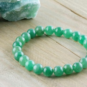 May include: A green gemstone bracelet made of round beads. The bracelet is on a light wood surface.