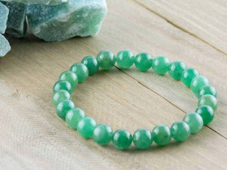 May include: A green gemstone bracelet made of round beads. The bracelet is on a light wood surface.