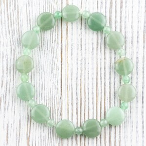 Peut inclure: Un bracelet en jade vert avec des perles rondes. Le bracelet est sur un fond en bois blanc.