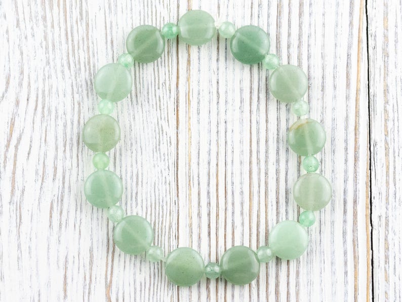 Peut inclure: Un bracelet en jade vert avec des perles rondes. Le bracelet est sur un fond en bois blanc.