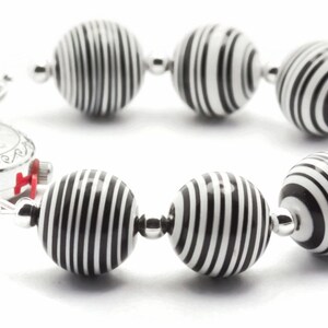 K&ouml;nnte beinhalten: Ein Armband aus schwarzen und wei&szlig;en Streifen mit einem silbernen Zifferblatt. Das Armband besteht aus runden Perlen mit einem schwarzen und wei&szlig;en Streifenmuster.
