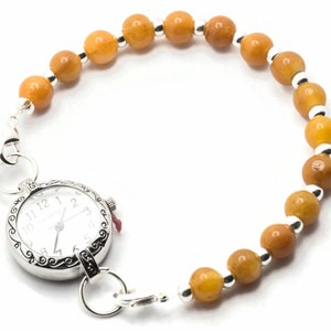 May include: A silver watch with a white face and black numbers is attached to a bracelet made of amber-coloured beads and silver spacers.