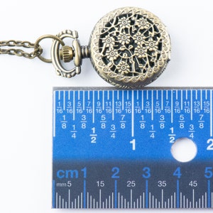 K&ouml;nnte beinhalten: Antike bronzefarbene Taschenuhr mit einem verzierten Blumendesign auf dem Deckel. Die Uhr ist an einer passenden Kette befestigt. Die Uhr hat einen Durchmesser von ca. 5 cm, wie auf dem Lineal gezeigt.