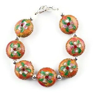May include: A bracelet with seven round beads, each with a floral design in shades of pink, green, and red on a peach background. The beads are connected by silver metal spacers.