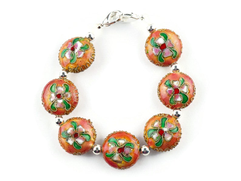 May include: A bracelet with seven round beads, each with a floral design in shades of pink, green, and red on a peach background. The beads are connected by silver metal spacers.