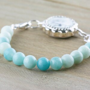 May include: A silver watch with a blue and green gemstone beaded bracelet.