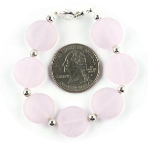 May include: A pink gemstone bracelet with silver beads and a silver clasp. The bracelet is about the size of a US quarter.