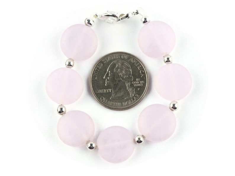 May include: A pink gemstone bracelet with silver beads and a silver clasp. The bracelet is about the size of a US quarter.