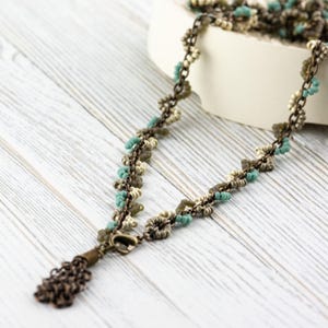 May include: A delicate necklace with a tassel made of small, turquoise, beige and brown beads. The necklace is made of metal and has a chain-like design.
