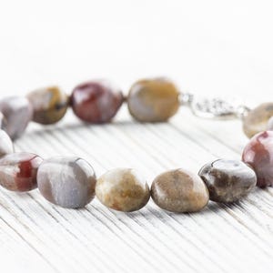 Op de afbeelding: Een armband gemaakt van bruine, witte en rode ovale stenen. De armband heeft een zilveren sluiting.