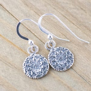 May include: A pair of silver dangle earrings with a delicate floral design. The earrings are made of sterling silver and have a hook closure.