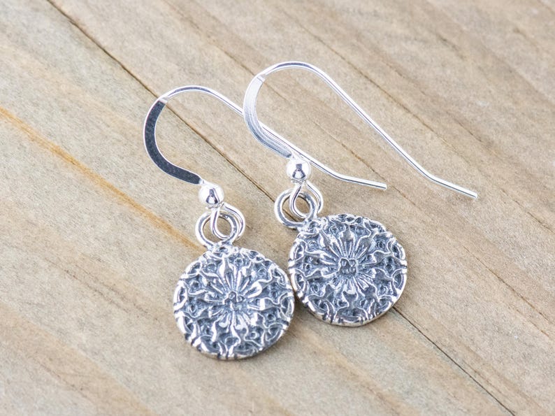 May include: A pair of silver dangle earrings with a delicate floral design. The earrings are made of sterling silver and have a hook closure.