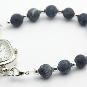 May include: A silver watch with a square face and black agate beads on a silver chain.