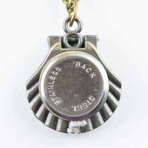 May include: The back of a silver pocket watch with a brass chain. The watch face says "BACK" and "STAINLESS STEEL".