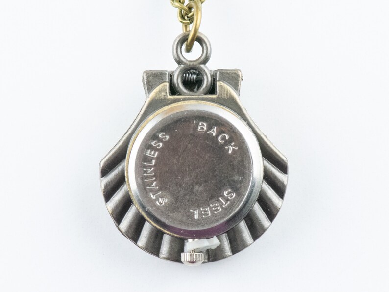 May include: The back of a silver pocket watch with a brass chain. The watch face says "BACK" and "STAINLESS STEEL".