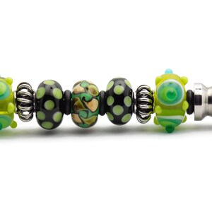 May include: A silver letter opener with a black and green glass bead handle. The beads are patterned with dots, swirls, and stripes.
