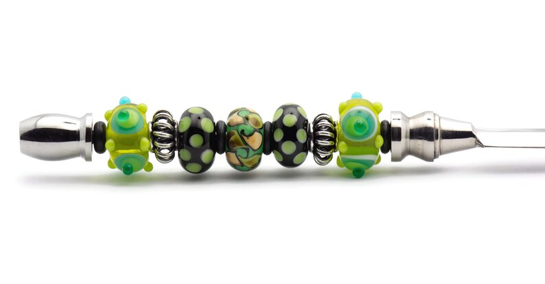 May include: A silver letter opener with a black and green glass bead handle. The beads are patterned with dots, swirls, and stripes.